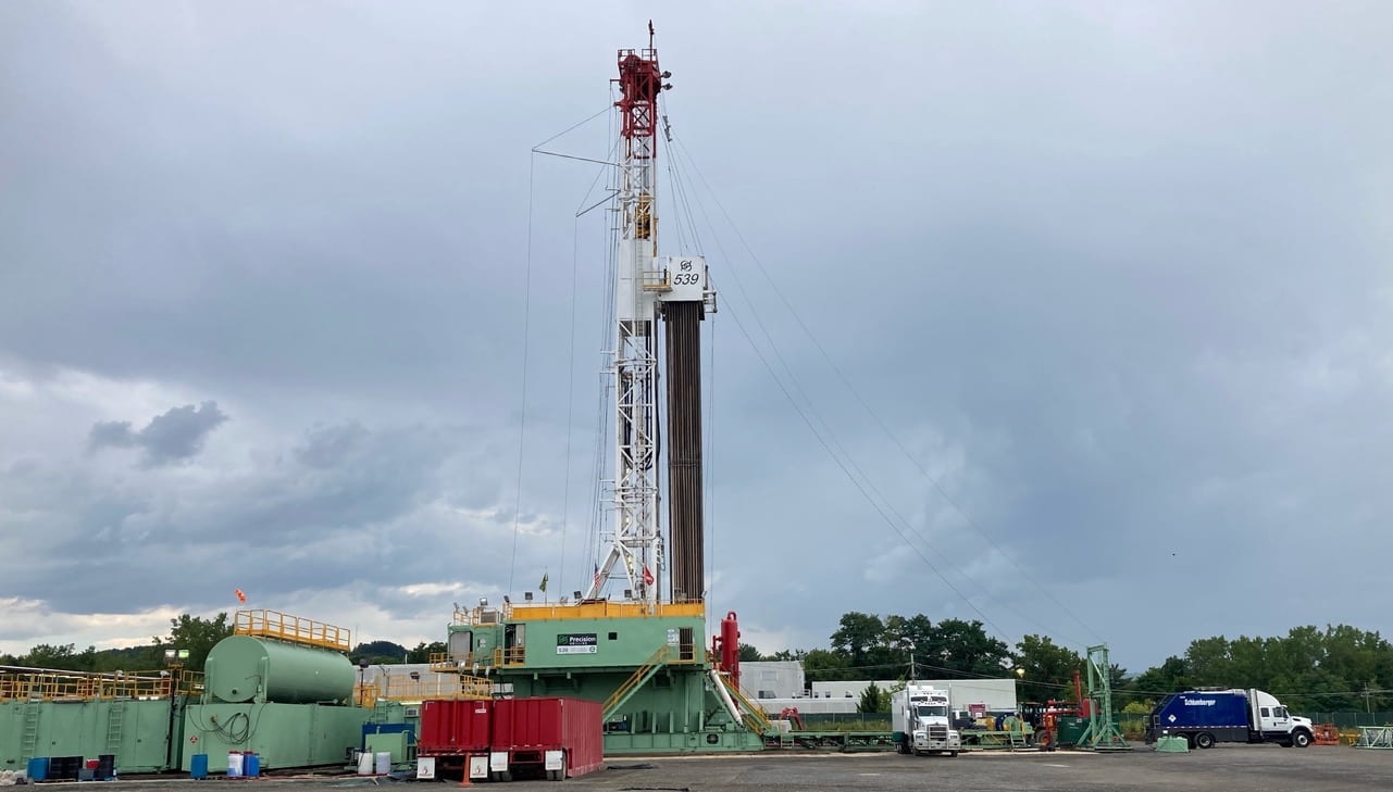 The wireline truck sits at one edge of the drill rig pad and feeds wire down the borehole.